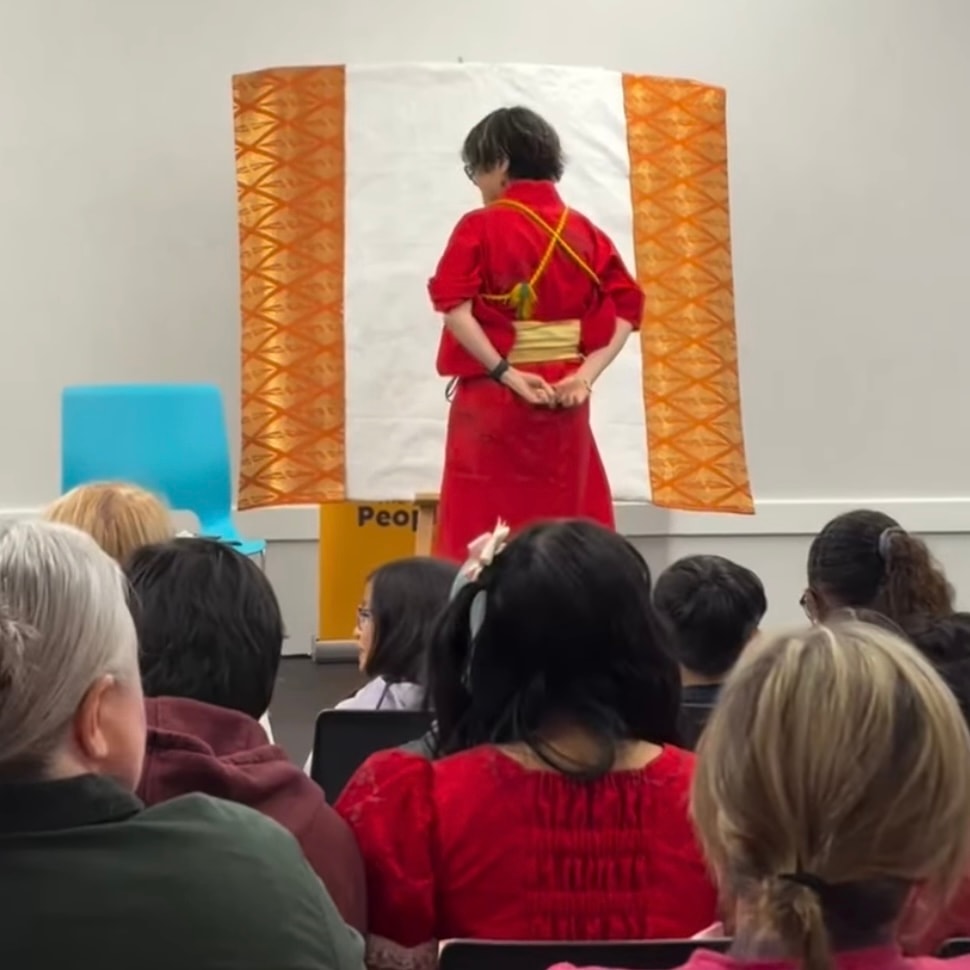 Chikako Ogawa in a red kimono performing a live ink brush painting demonstration for an audience