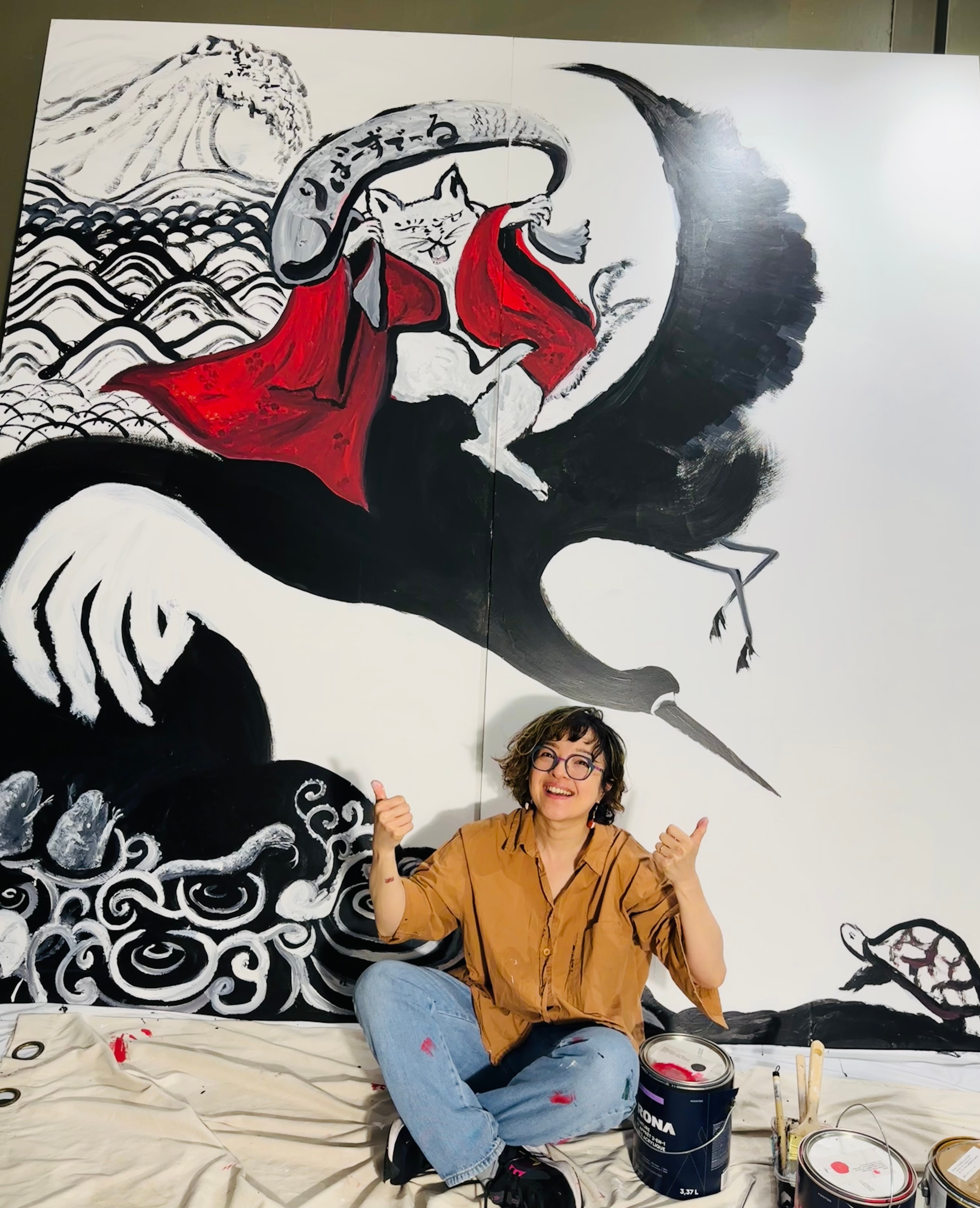 Chikako Ogawa posing in front of a large hand-painted mural of a cat riding a crane