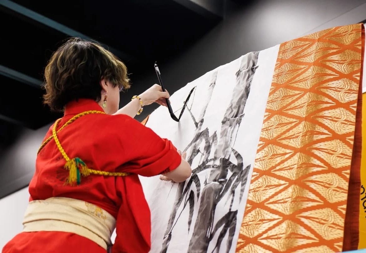Chikako Ogawa in a red kimono hand-painting a large ink brush illustration on fabric