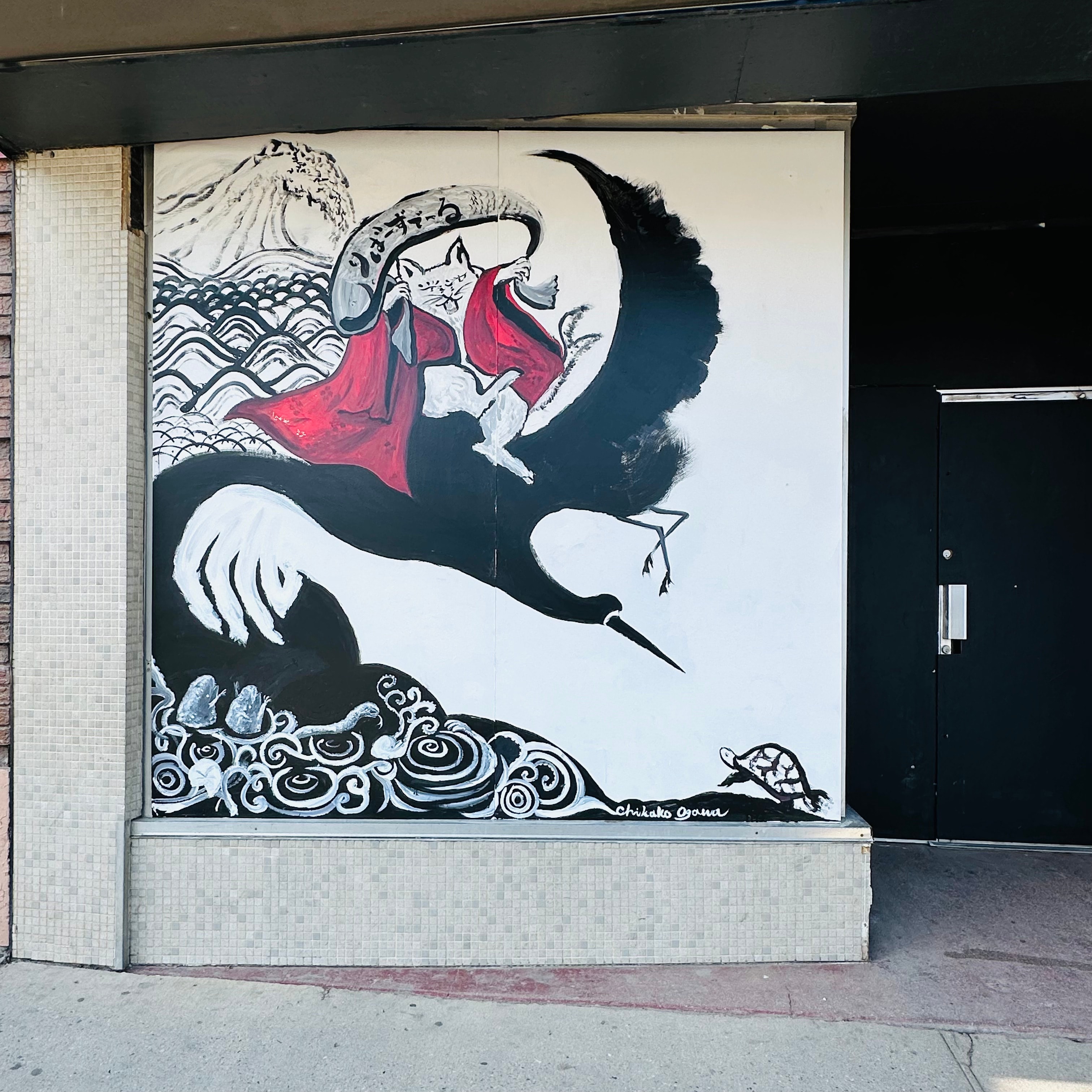 Black and white mural of a cat riding a crane over ocean waves and a turtle